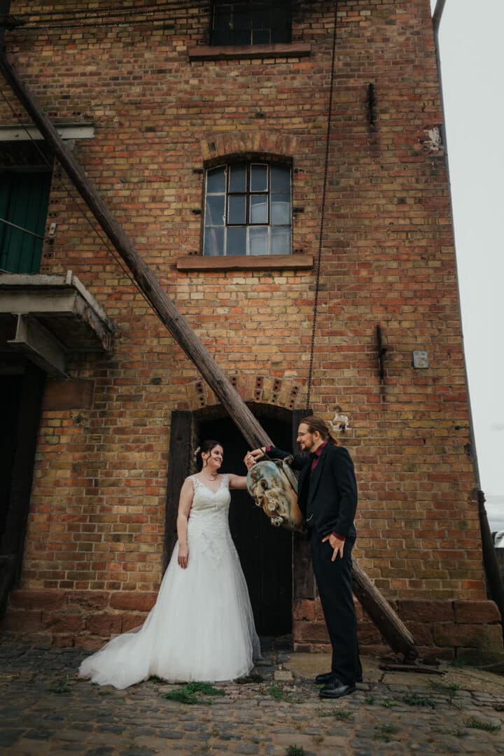 Brautpaar lehnt an einem alten Balken an vor einem alten Hofgut Gebäude